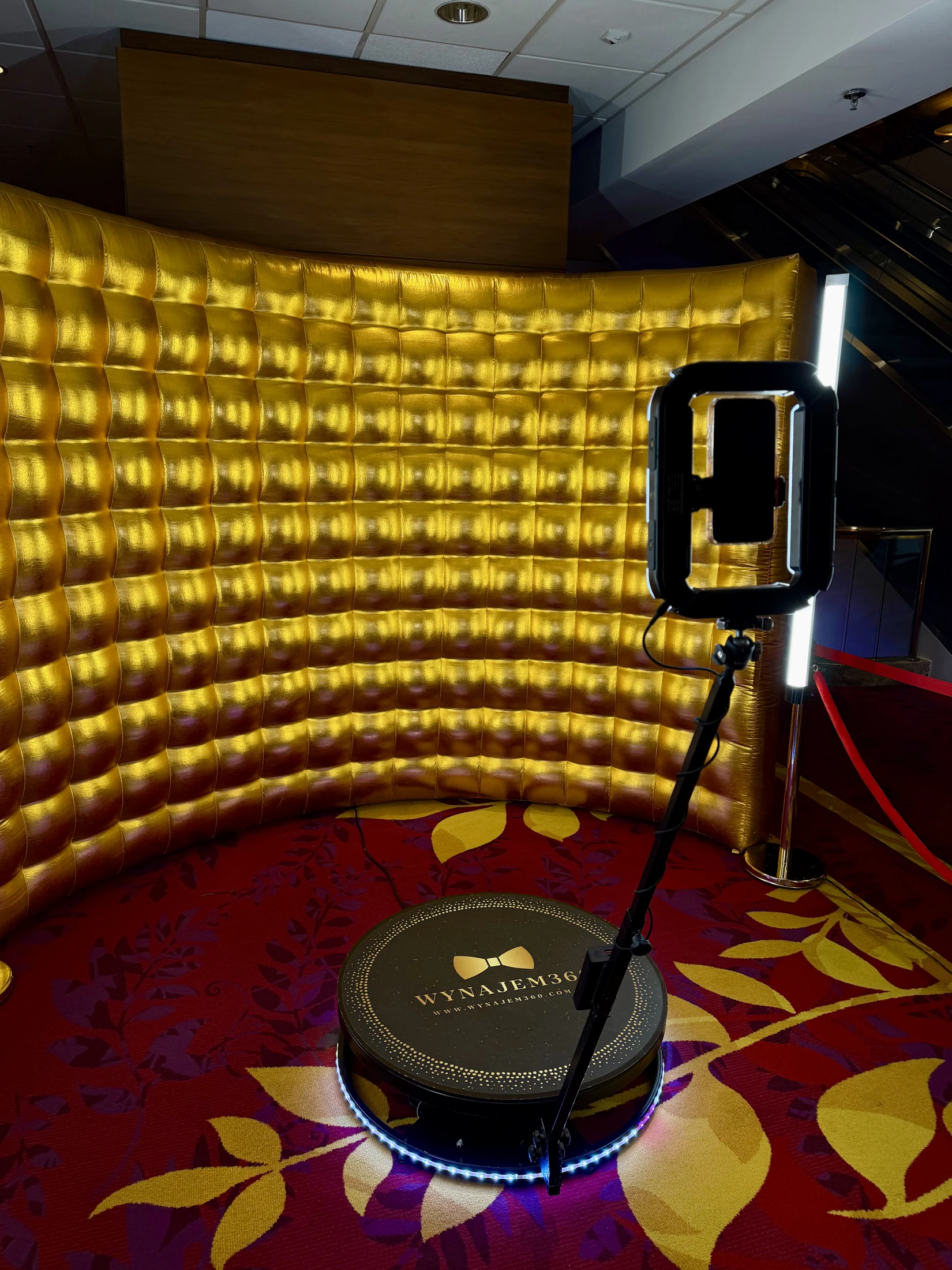 Fotobudka 360 ze złotą ścianką i oświetleniem w sali eventowej