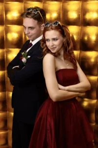 Goście weselni pozują do zdjęcia w klasycznej fotobudce na tle eleganckiej złotej ścianki fotograficznej.